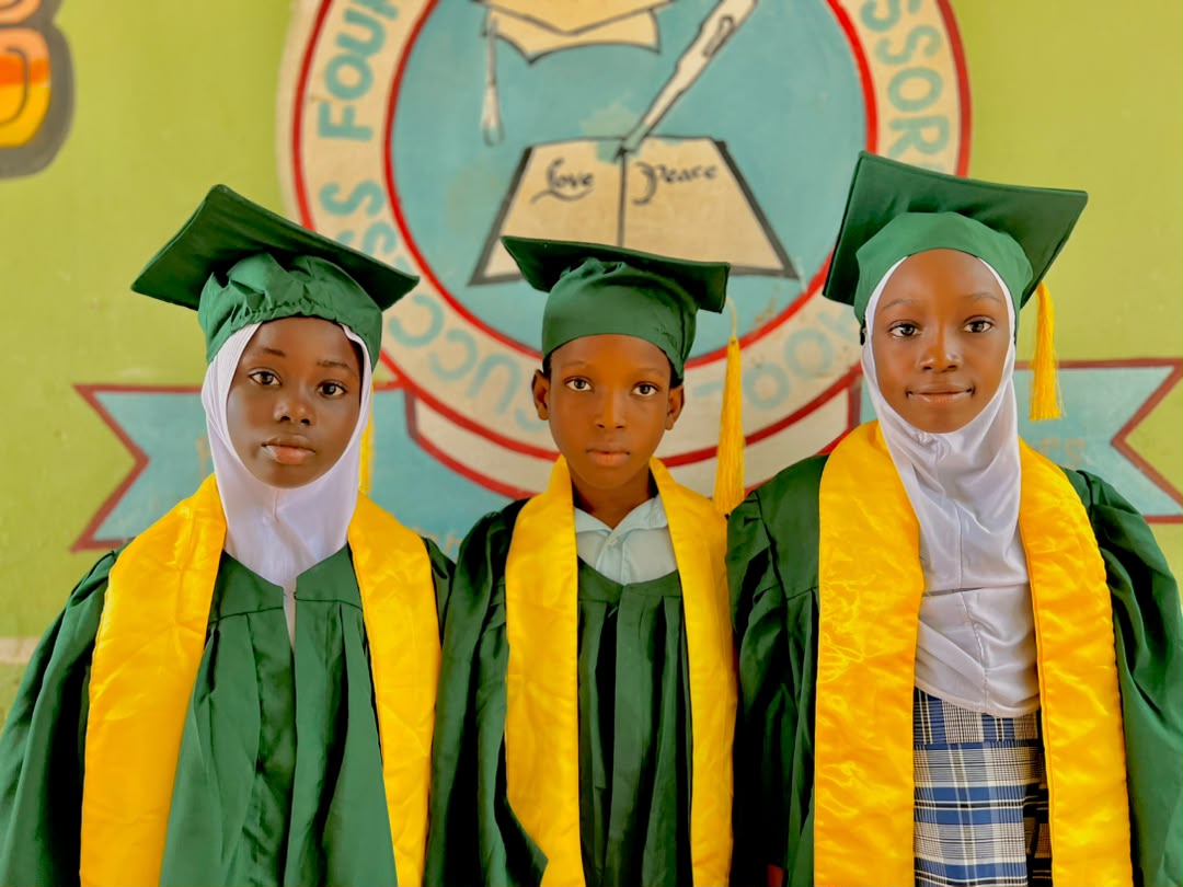 Three SFMS 2025/2026 graduands in green and gold gowns before the school crest